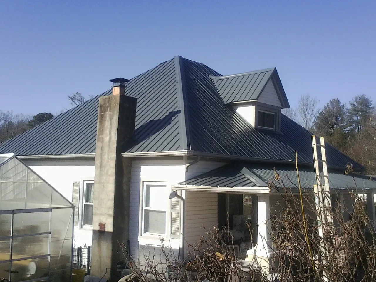 Dark blue standing seam metal roof on a white farmhouse with dormer — Slate & Tile Roof Repair by Roofing Brothers in Campus