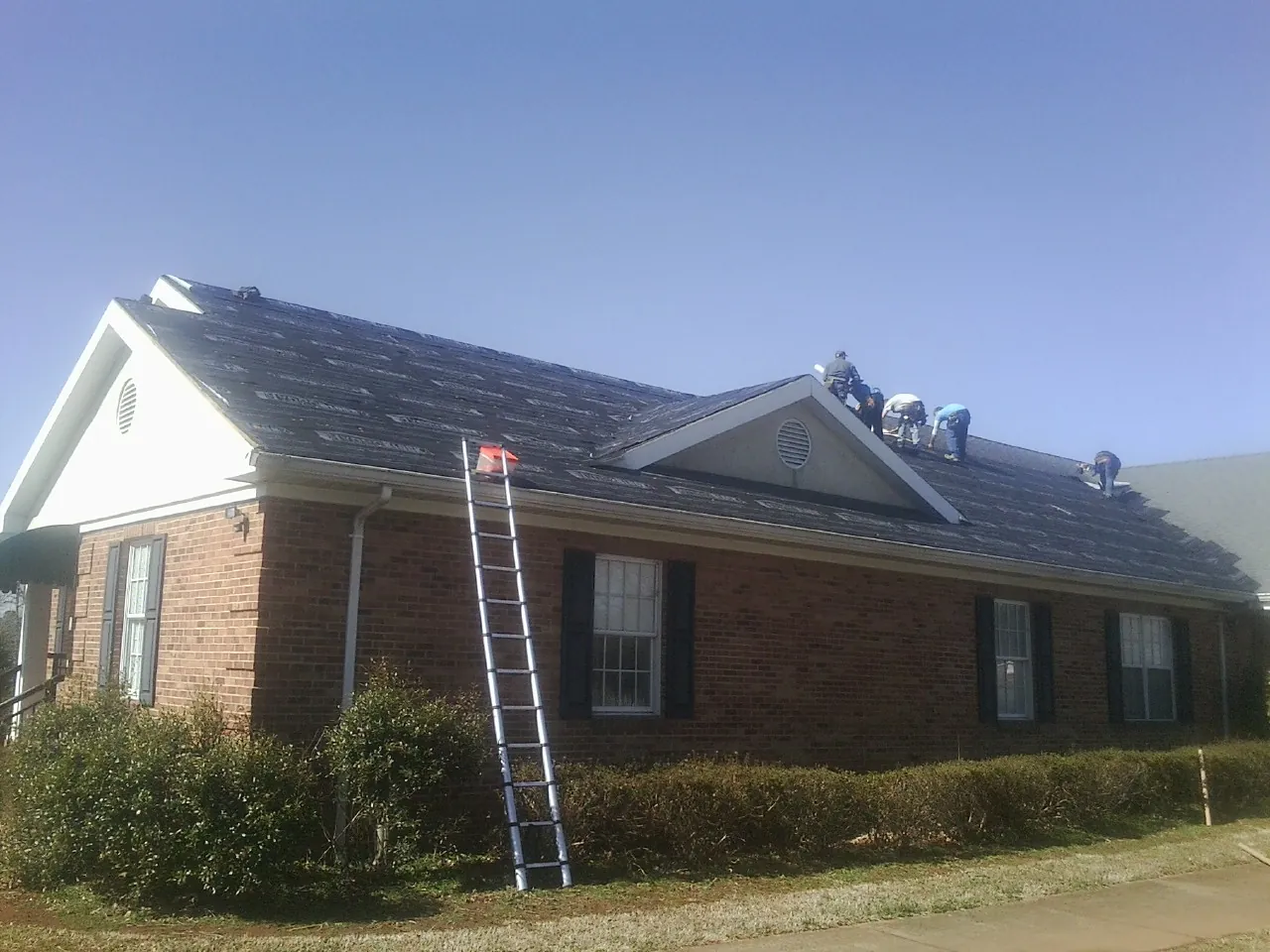 Crew tearing shingles off a brick ranch roof with a ladder set — Metal Roof Repair work by our crew in Campus