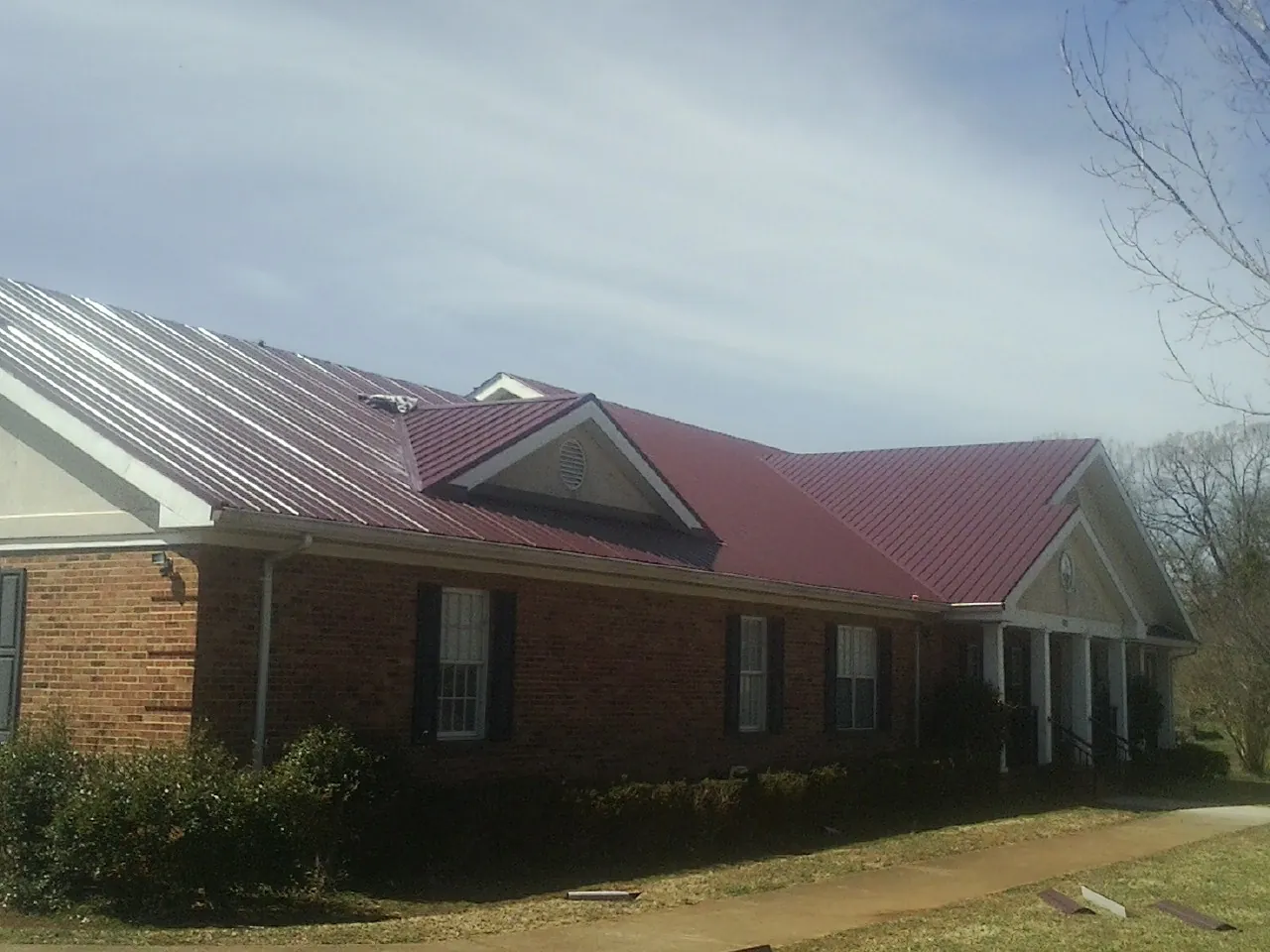Red metal roof with gabled entries on a long brick building, from a Hail Damage Roof Repair job in Campus