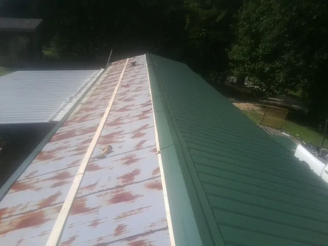 Old rusted panels beside newly installed green metal roofing — Wind Damage Roof Repair by Roofing Brothers in Campus