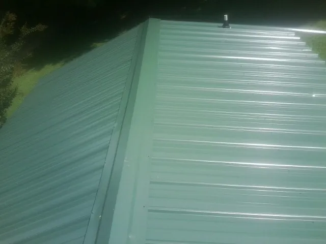 New green metal panels meeting at the ridge of a roof — Flat Roof Repair work by our crew in Campus