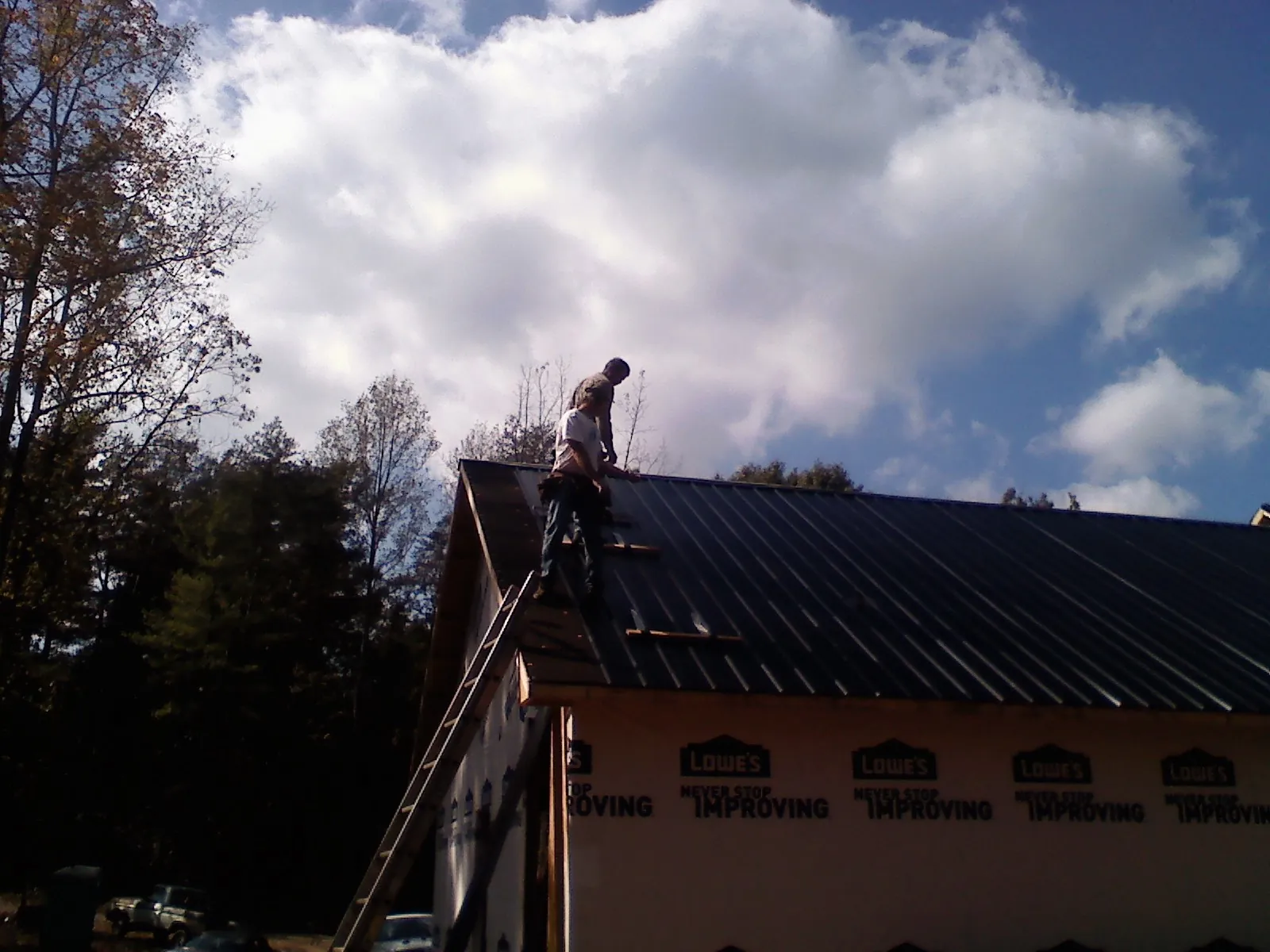 Roofer fastening dark metal panels high against a cloudy sky, from a Roof Inspection job in Campus